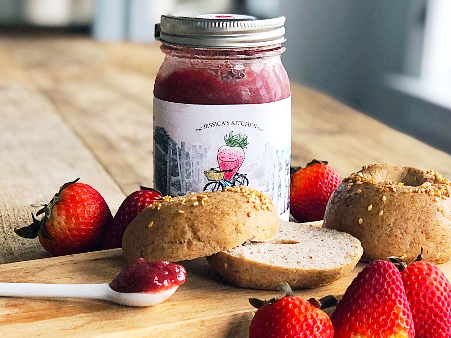 Strawberry jam packaging with bagels and strawberries in front