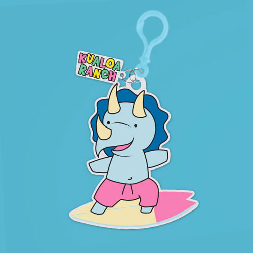 PVC keychain of a blue triceratops with pink swim trunks on a surfboard